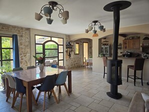 Un vaste espace dédié à la salle à manger, avec une grande table et des chaises, un mur en pierre et une cuisine dotée de meubles en bois.