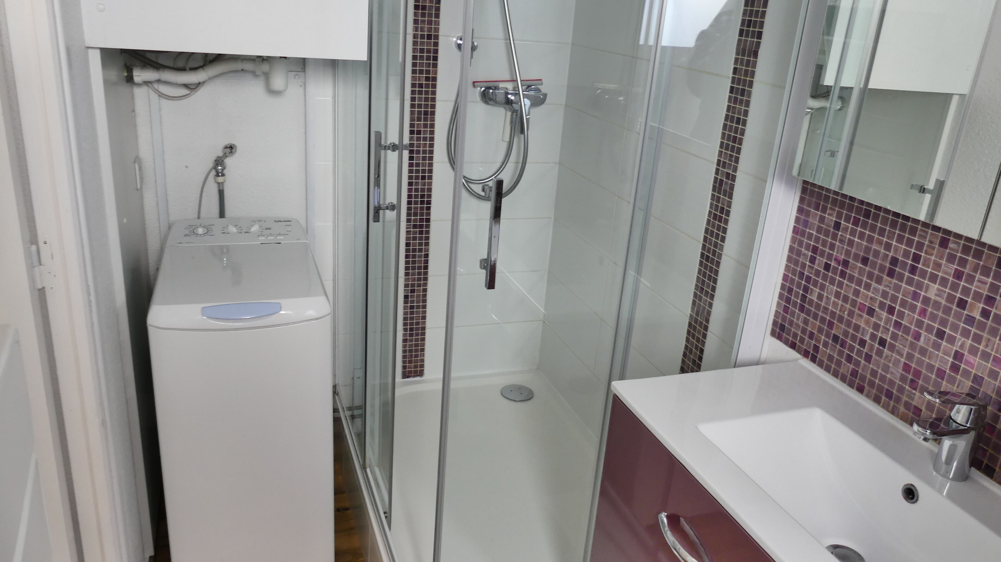 A compact bathroom with a glass-enclosed shower, a white sink, and a washing machine.