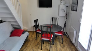 A compact living space with a white sofa, red cushions, a round table with chairs, a staircase, and a radiator.