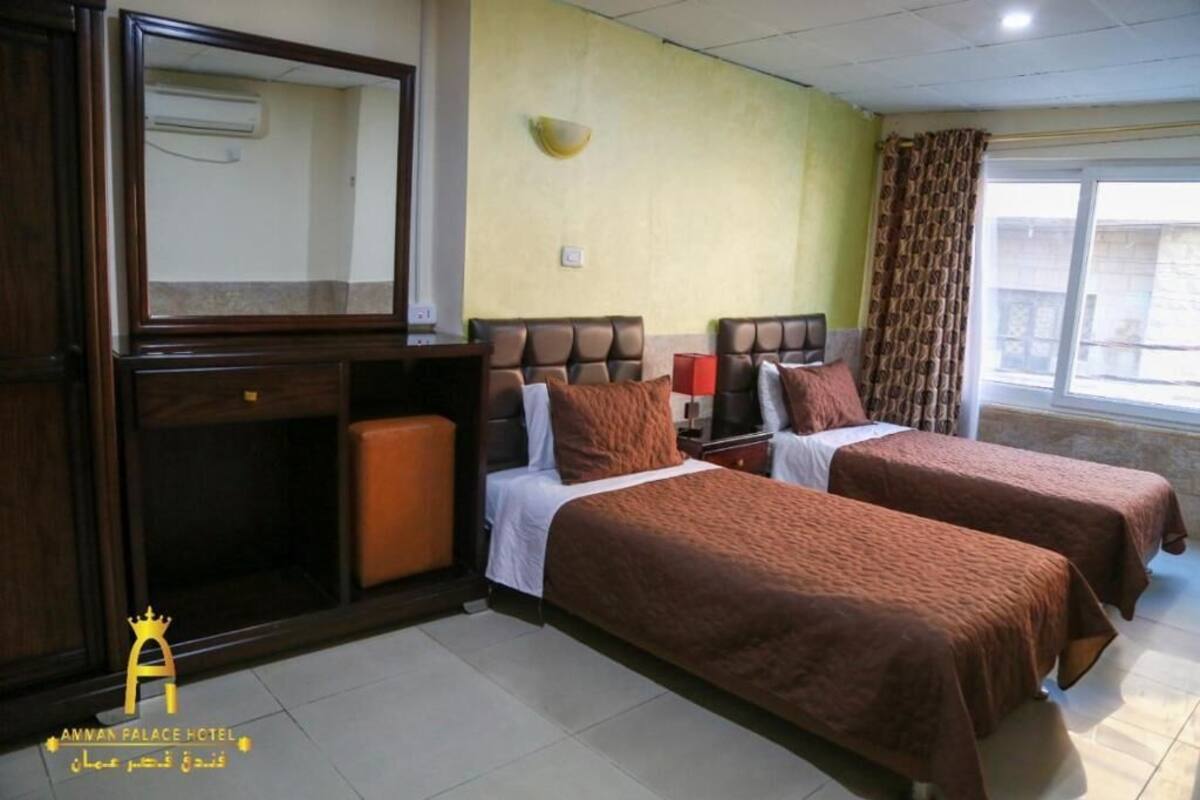 Quarto de hotel com duas camas, um espelho, uma mesinha e uma janela com cortinas.