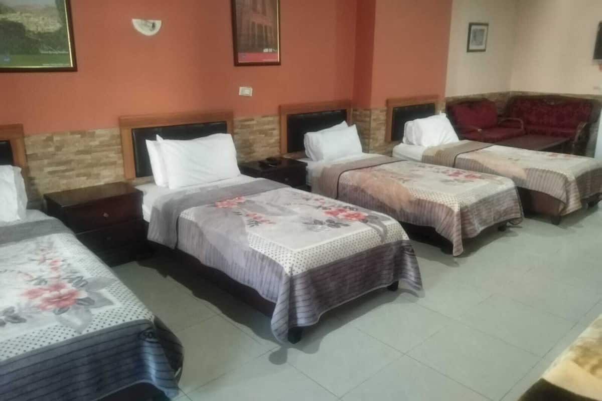 Quarto de hotel com três camas de solteiro, um sofá e uma pequena mesa.