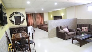 Um saguão de hotel com área de refeições, dois sofás, uma mesa de centro e uma TV fixada na parede.
