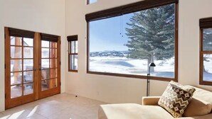 A room with a large window offering a snowy landscape view, a sliding glass door, and a beige sofa with a patterned pillow.