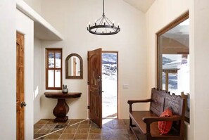 Stunning hallway with a chandelier, comfortable bench, and a mirror, leading to an outdoor area with a scenic view.