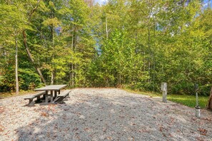A picnic area with a wooden table and benches, surrounded by trees and gravel ground. - RV Site 1 of 4: Lot rental only; RVs not provided. (South Bloomingville)