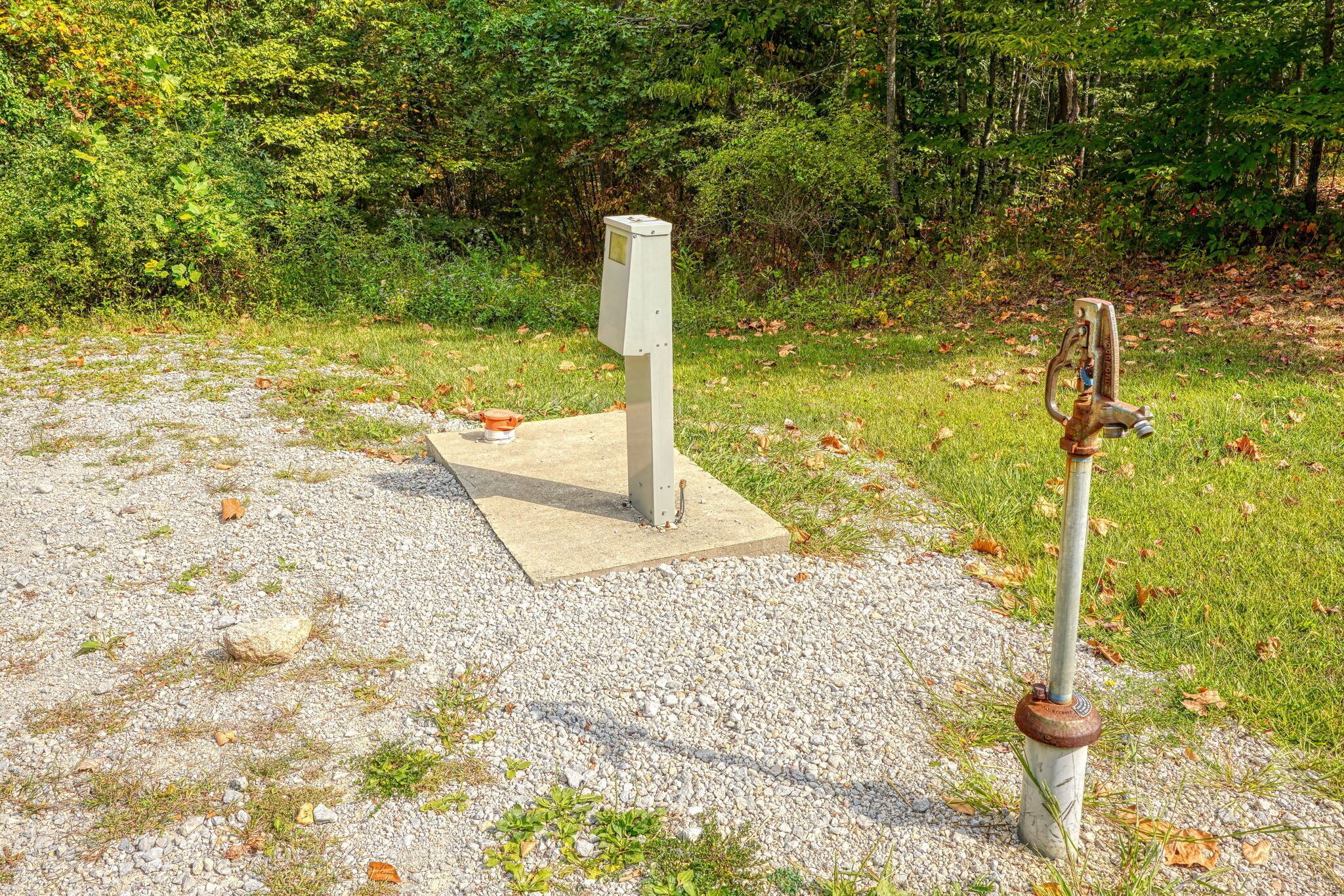 A concrete structure with a metal object on a gravel surface, surrounded by grass and trees.