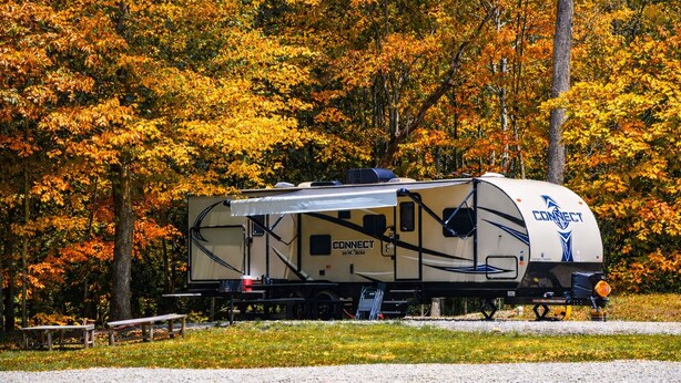 A recreational vehicle (RV) with the brand name 'CONNECT' parked in a park with autumn foliage. - RV Site 4 of 4: Lot rental only; RVs not provided. (South Bloomingville)
