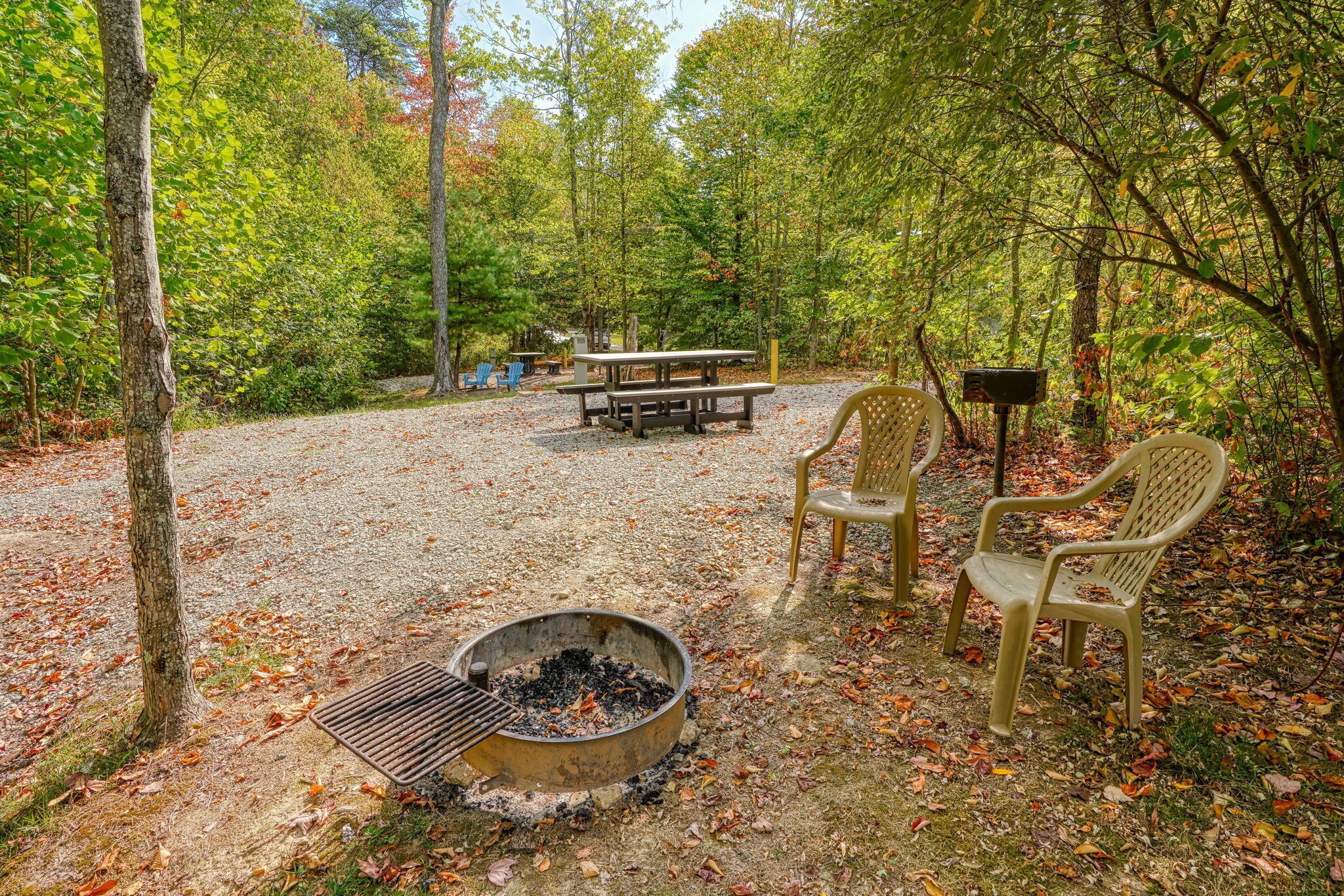A campsite with a fire pit, picnic table, and chairs.