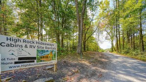 A sign for High Rock Hideaways Cabins & RV Site Rentals with a forested backdrop. - RV Site 4 of 4: Lot rental only; RVs not provided. (South Bloomingville)