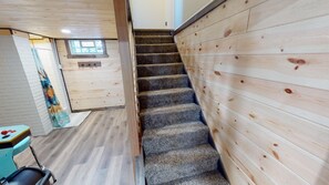 Una escalera con paredes de madera y peldaños alfombrados que conduce a una habitación con ventana y una pequeña mesa.