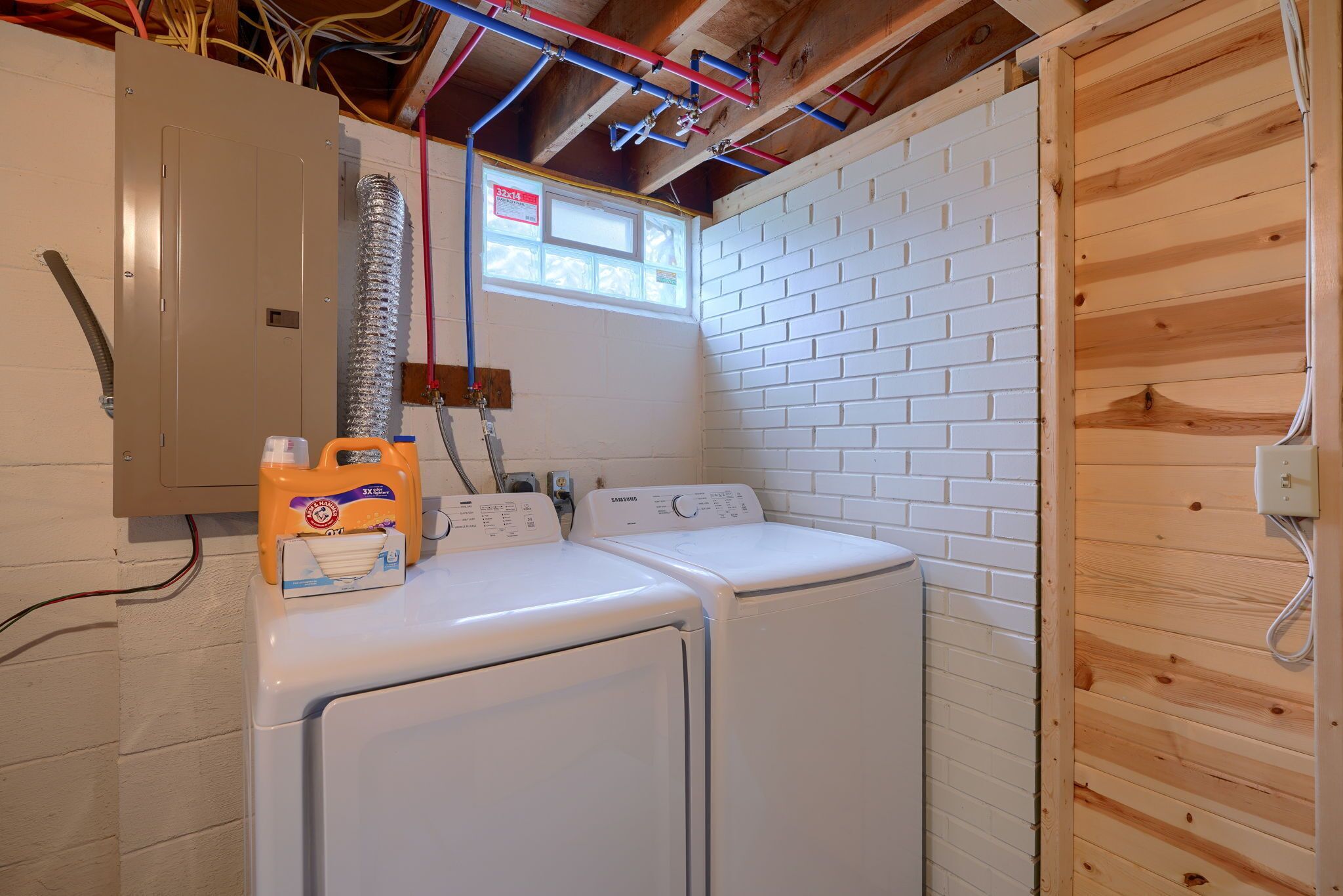 A laundry room with two white washing machines, a metal utility cabinet, and a window with a view of the outside.