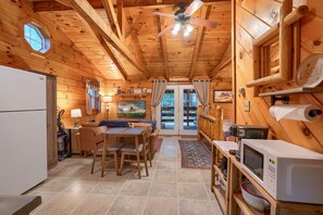 L’intérieur d’une cabane en bois comprend un coin repas, une cuisine et une grande fenêtre.