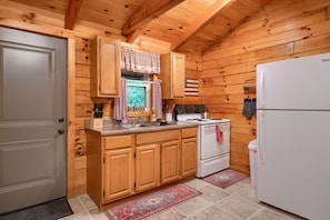 Une cuisine rustique aménagée dans une cabane en bois, avec un poêle, un réfrigérateur et des placards en bois.
