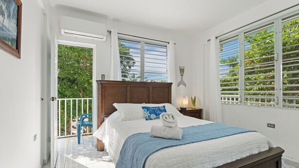 Un dormitorio con una cama grande, cabecera de madera, balcón con una silla azul y vistas a la vegetación.