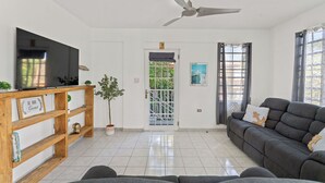 Una sala de estar con televisor de pantalla plana, ventilador de techo, sofá y estante de madera con un cartel.