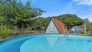 Una piscina con cubierta de madera, rodeada de árboles y un pequeño edificio con techo rojo.