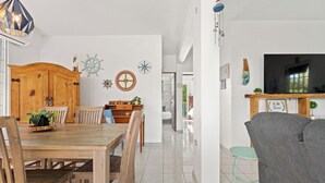 Un salón amplio con una mesa de comedor de madera, un sofá gris y un televisor montado en la pared.