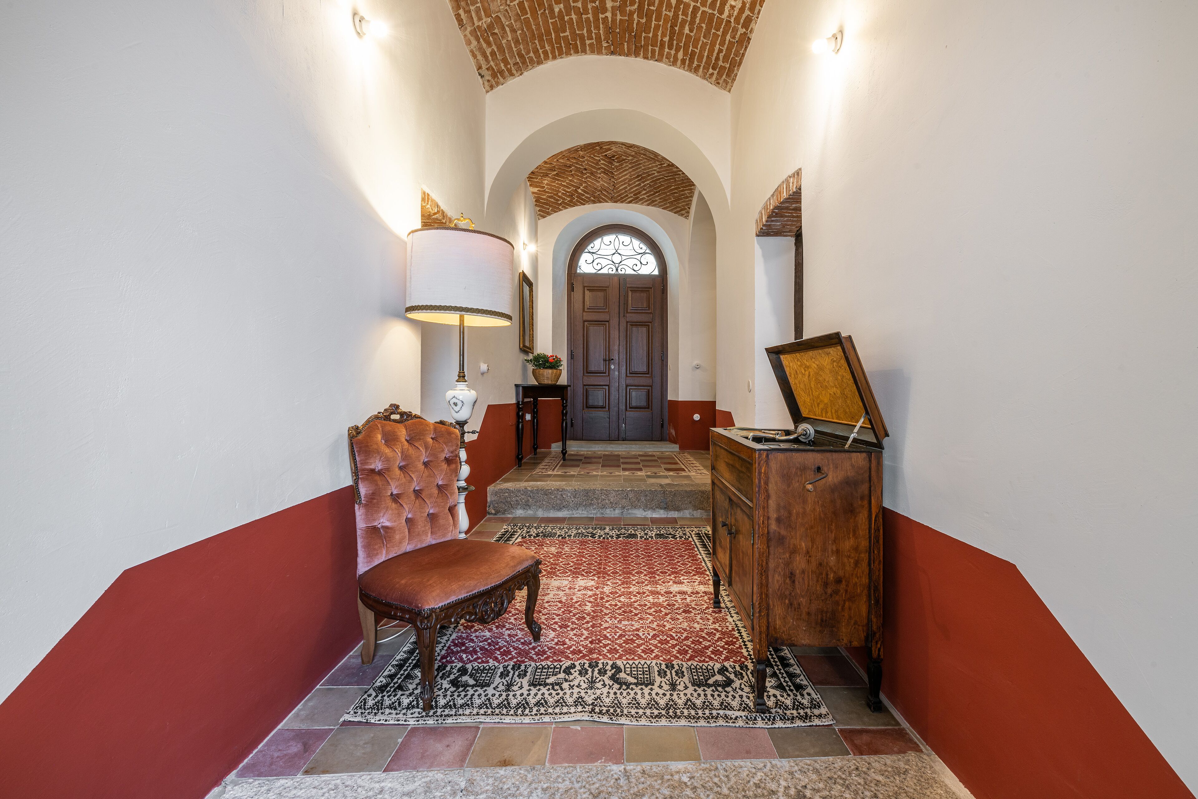 A hallway with a red and white wall, a wooden bench, a wooden dresser, and a patterned rug.