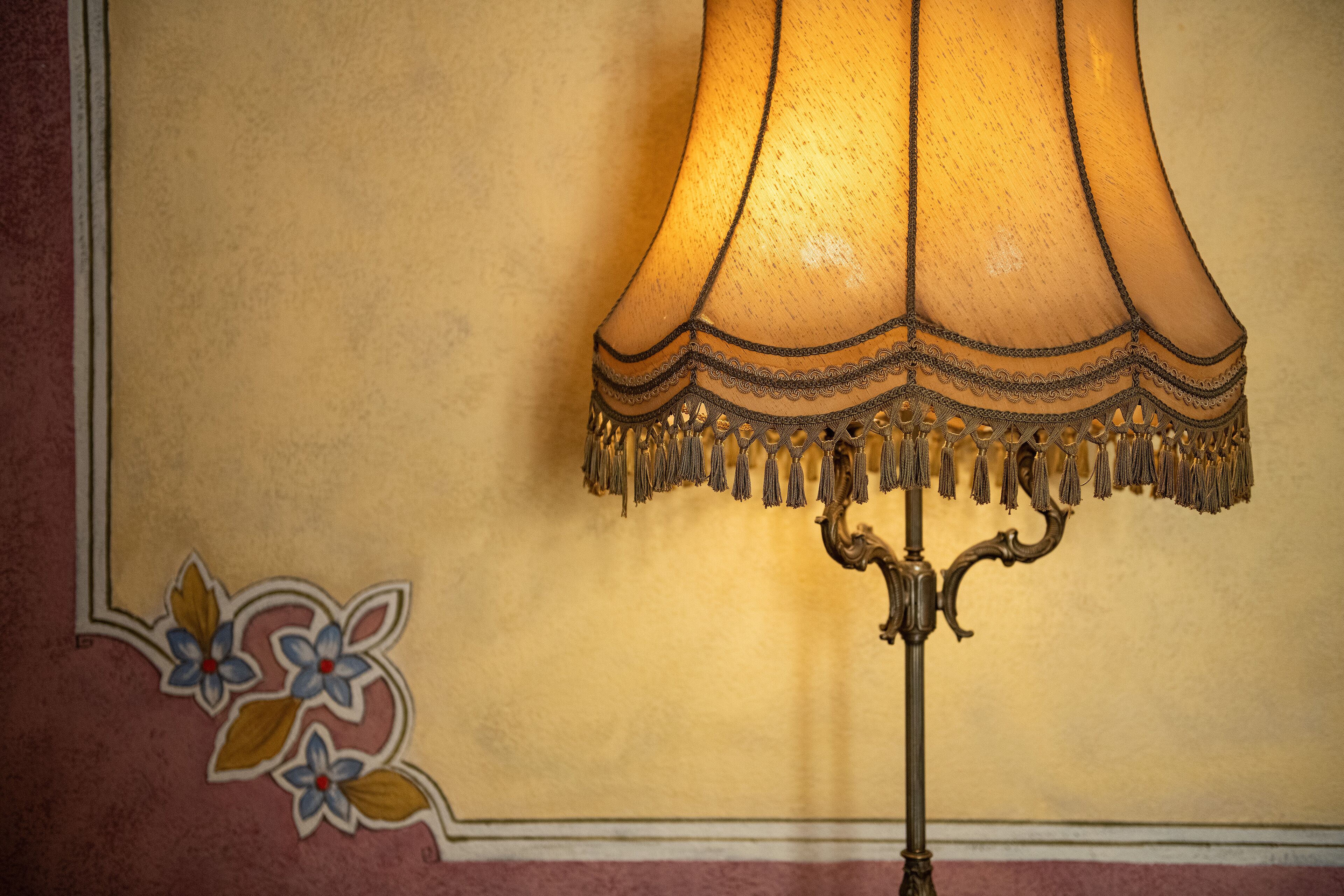 Une lampe dotée d’un abat-jour décoratif et de franges, placée contre un mur orné de motifs floraux.