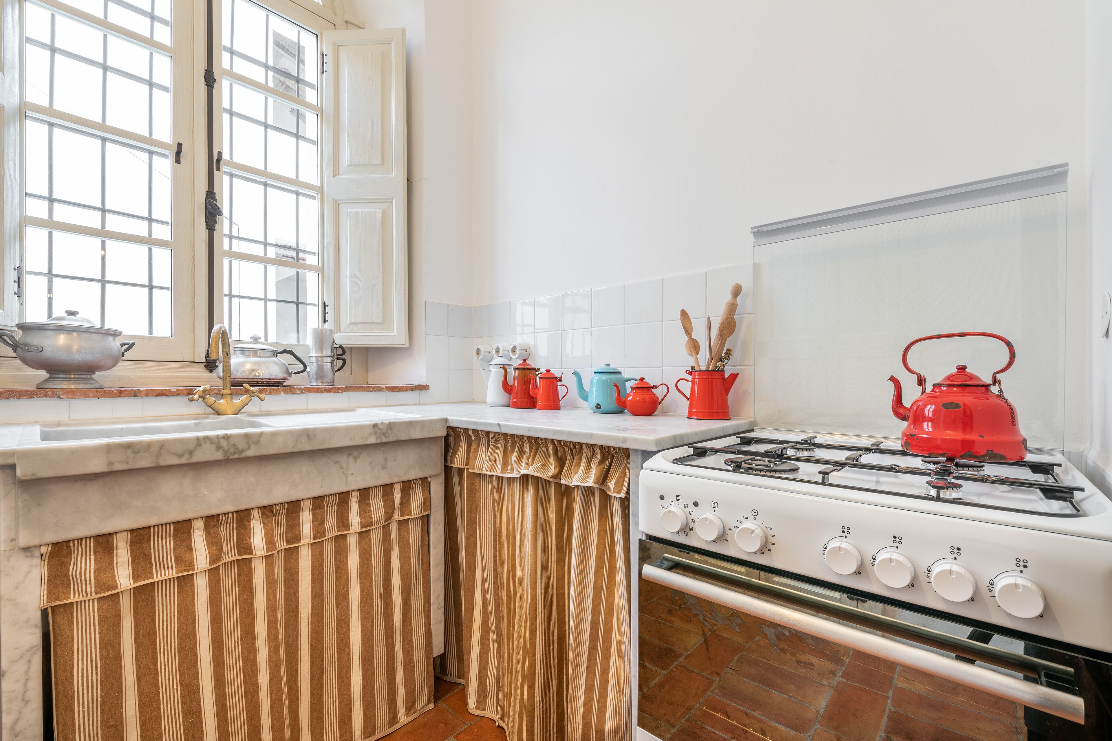 A kitchen with a gas stove, a sink, and a window with curtains.
