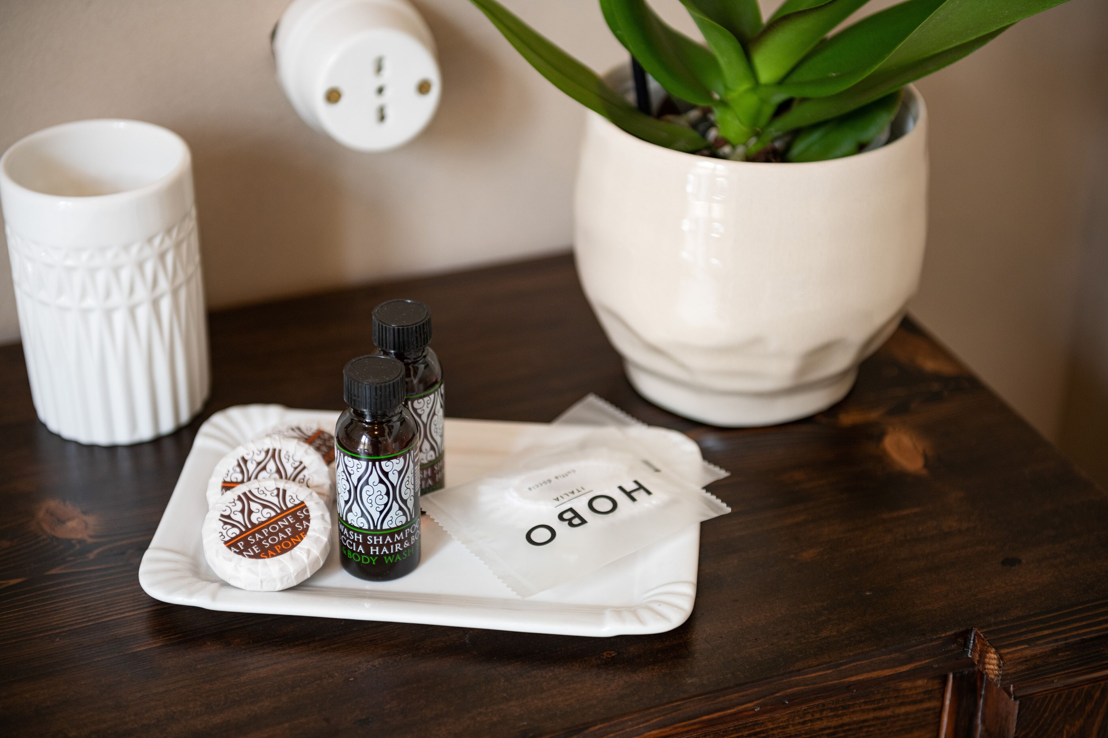 A tray with a bar of soap, a bottle of shampoo, and a packet of hair oil on a wooden table.