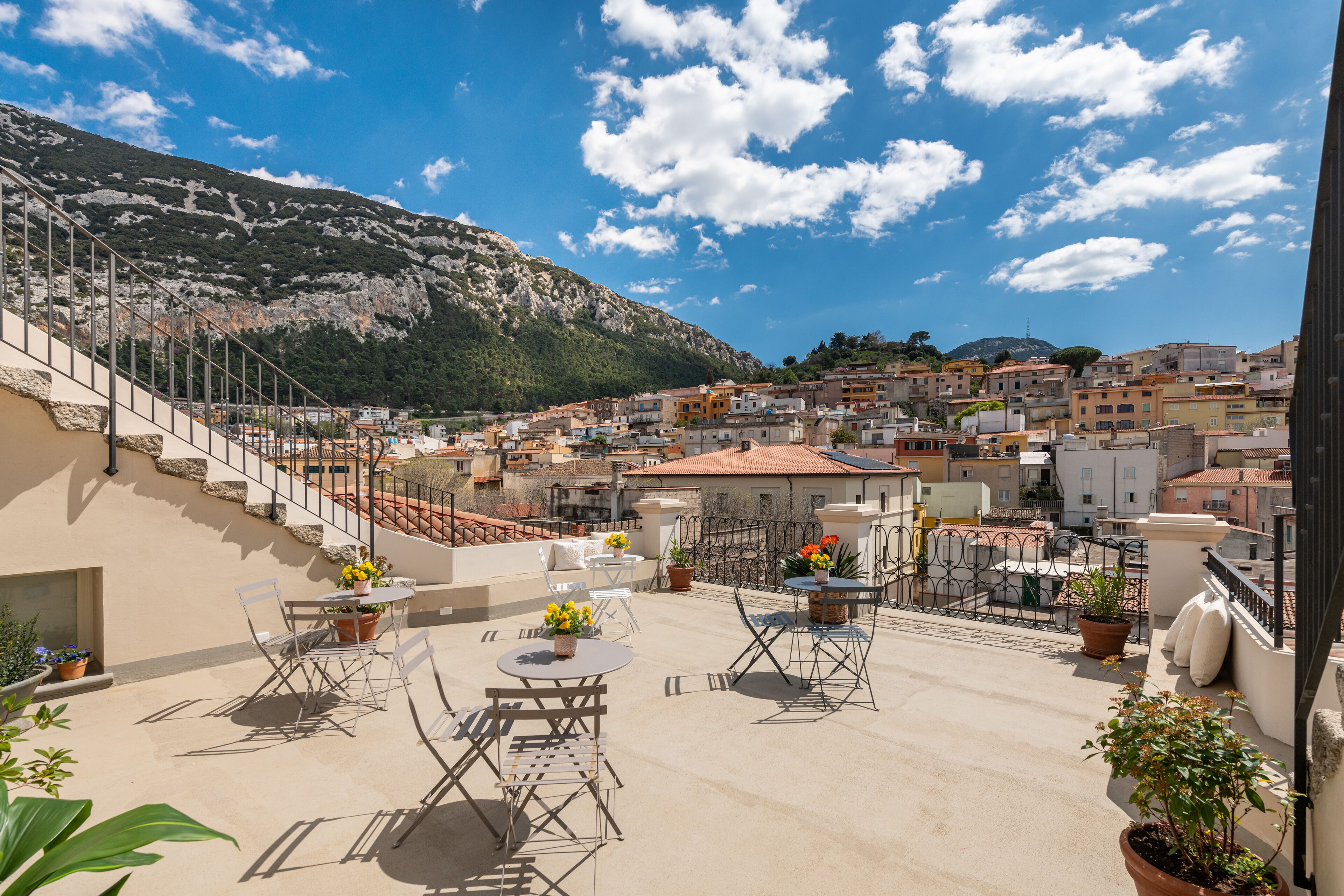 Terraza en la azotea con mobiliario exterior, plantas en macetas y vistas a un pueblo montañoso.