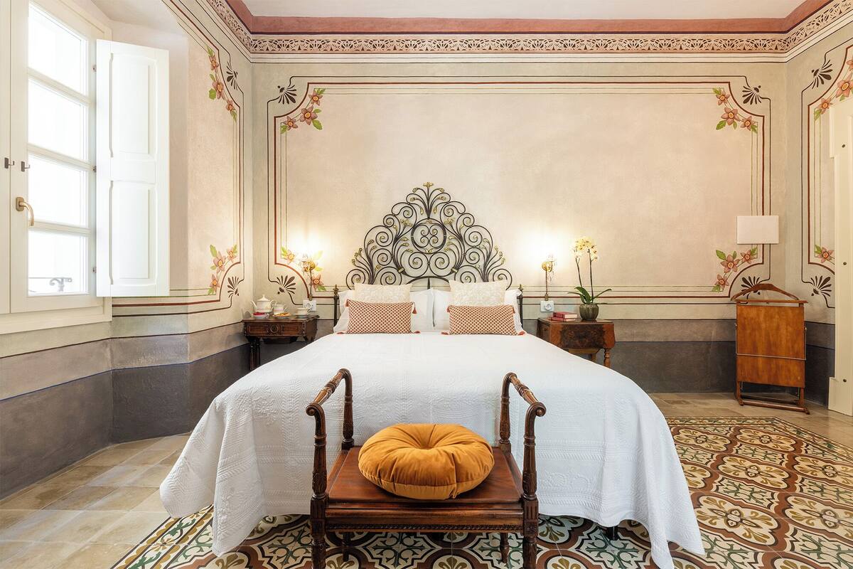 A spacious bedroom with a large bed, ornate headboard, and a decorative floor pattern.