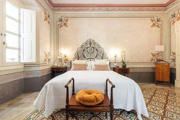 A spacious bedroom with a large bed, ornate headboard, and a decorative floor pattern. - Palazzo Cherchi (Dorgali)