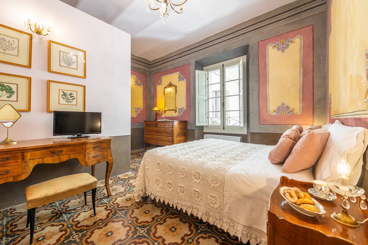 A room with a bed, a desk, a chair, a television, and a nightstand with a lamp and a plate of food.