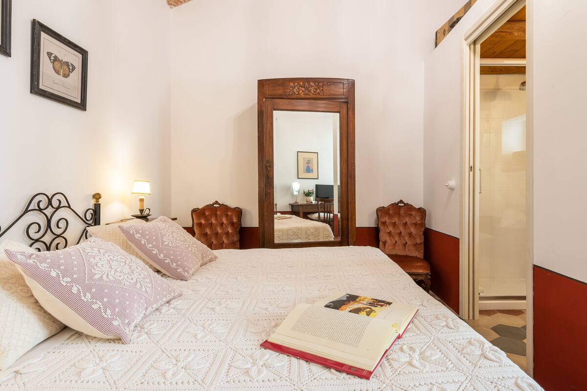 A bedroom with a large bed, a wooden headboard, a mirror, and a door leading to a bathroom.