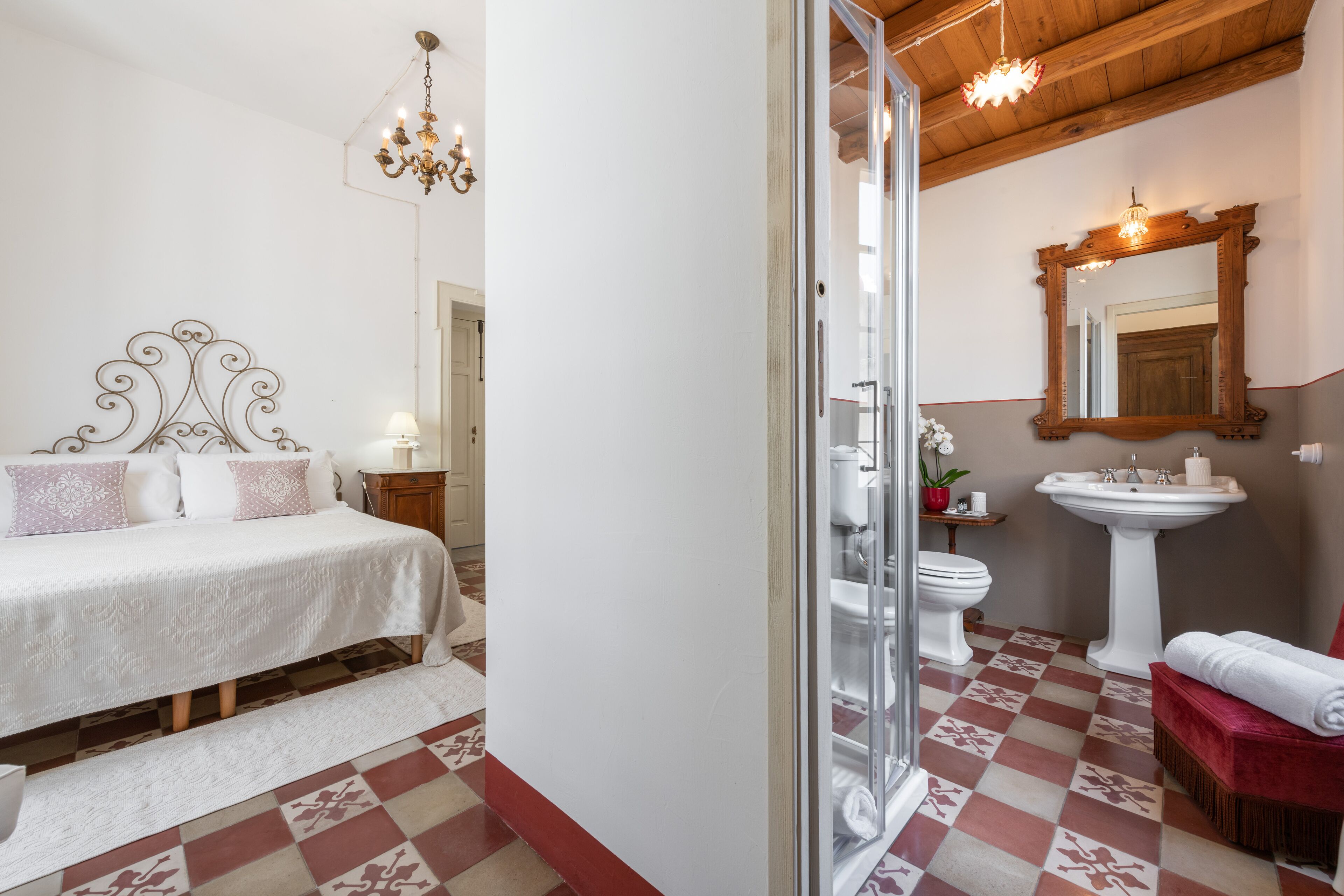 Een slaapkamer met een bed, een nachtkastje en een toilet. Er is een badkamer met een wastafel, een spiegel en een toilet.
