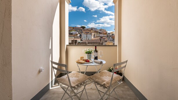 Een balkon met een tafel gedekt voor twee personen, een fles wijn en een vaas met bloemen.