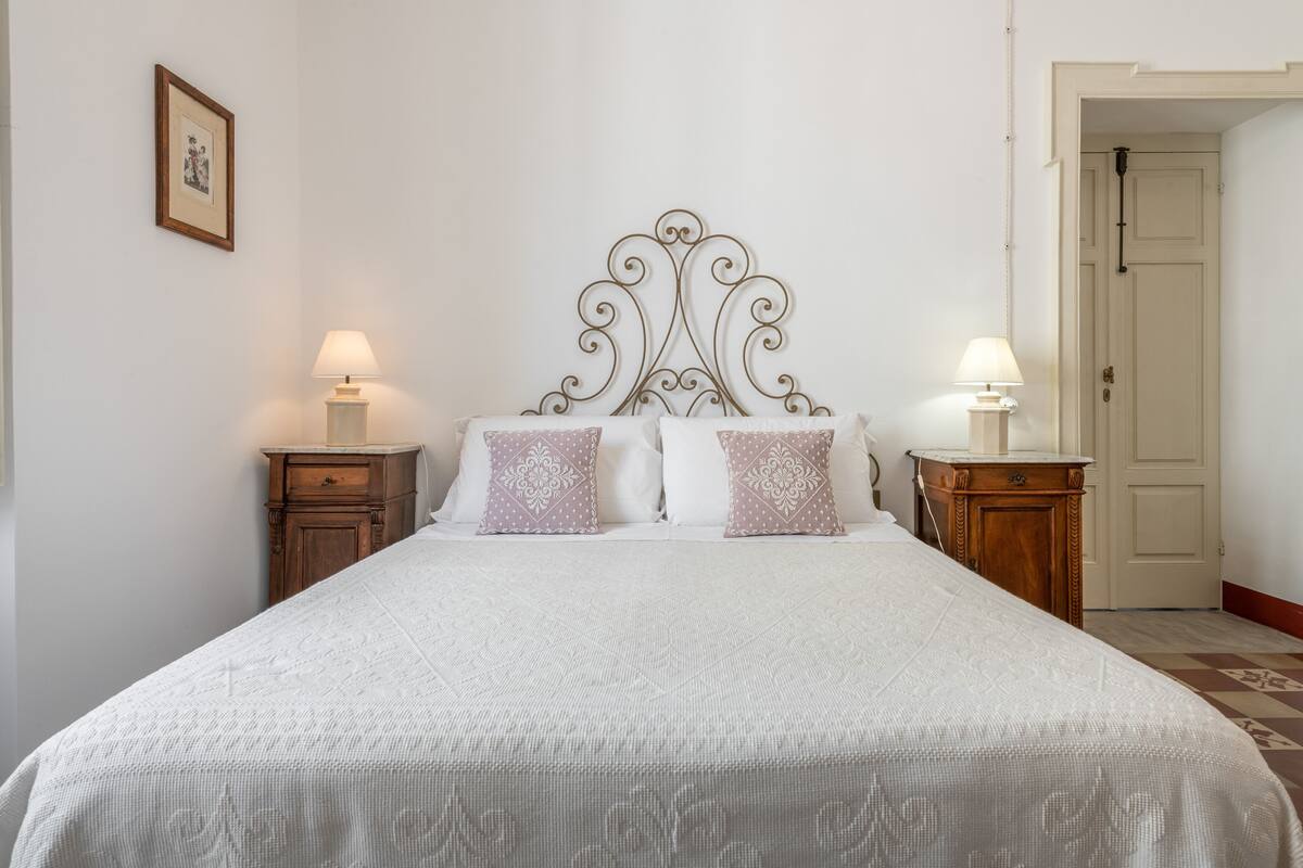A neatly made bed with a decorative headboard, two bedside tables with lamps, and a framed picture on the wall.