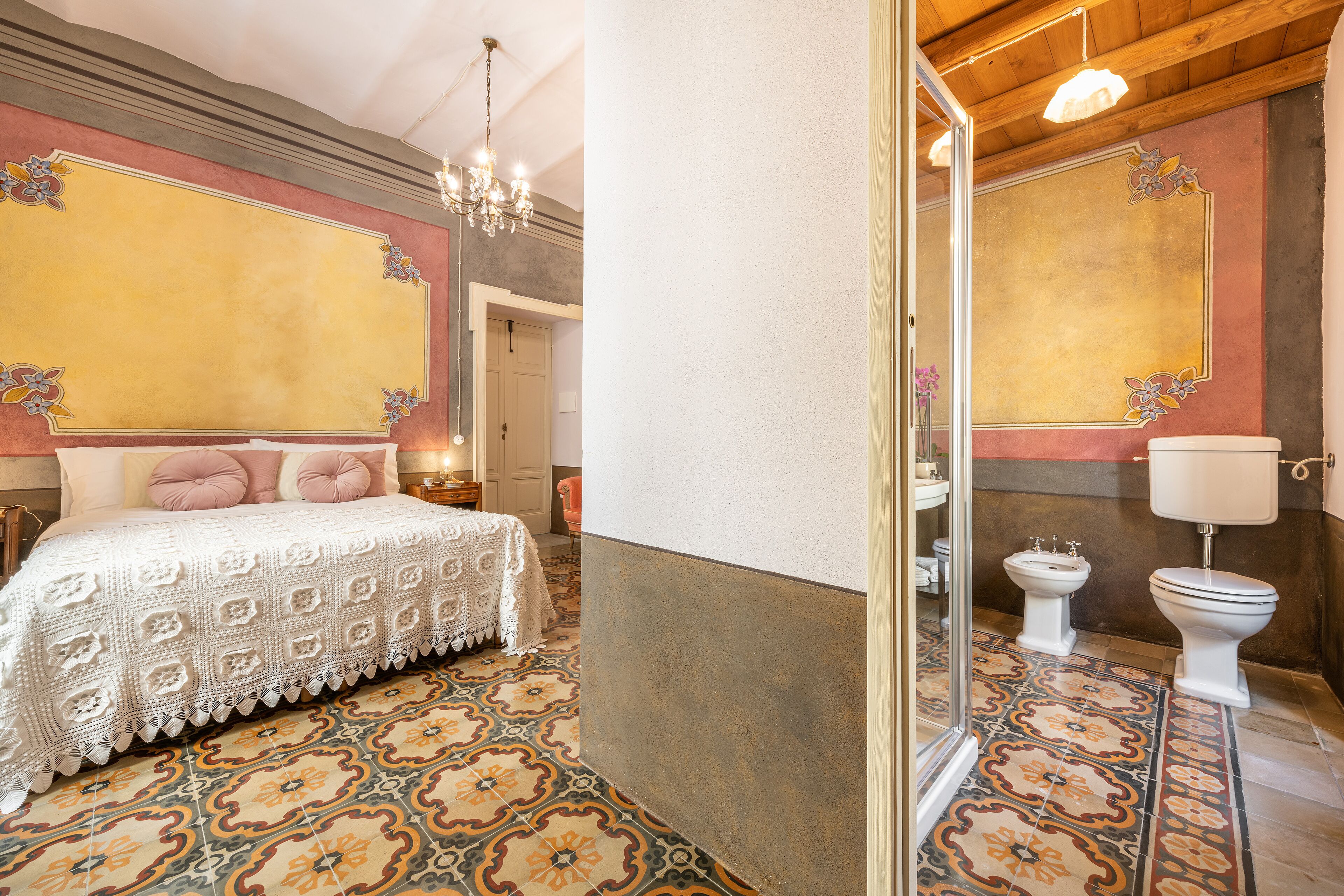 Un dormitorio con una cama grande, un candelabro y un baño con dos inodoros y un espejo.