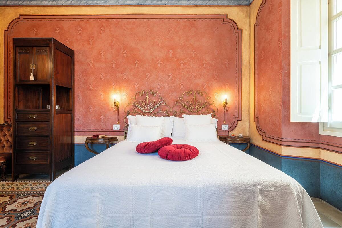 A hotel room with a large bed, two bedside tables, a wardrobe, and a patterned rug.