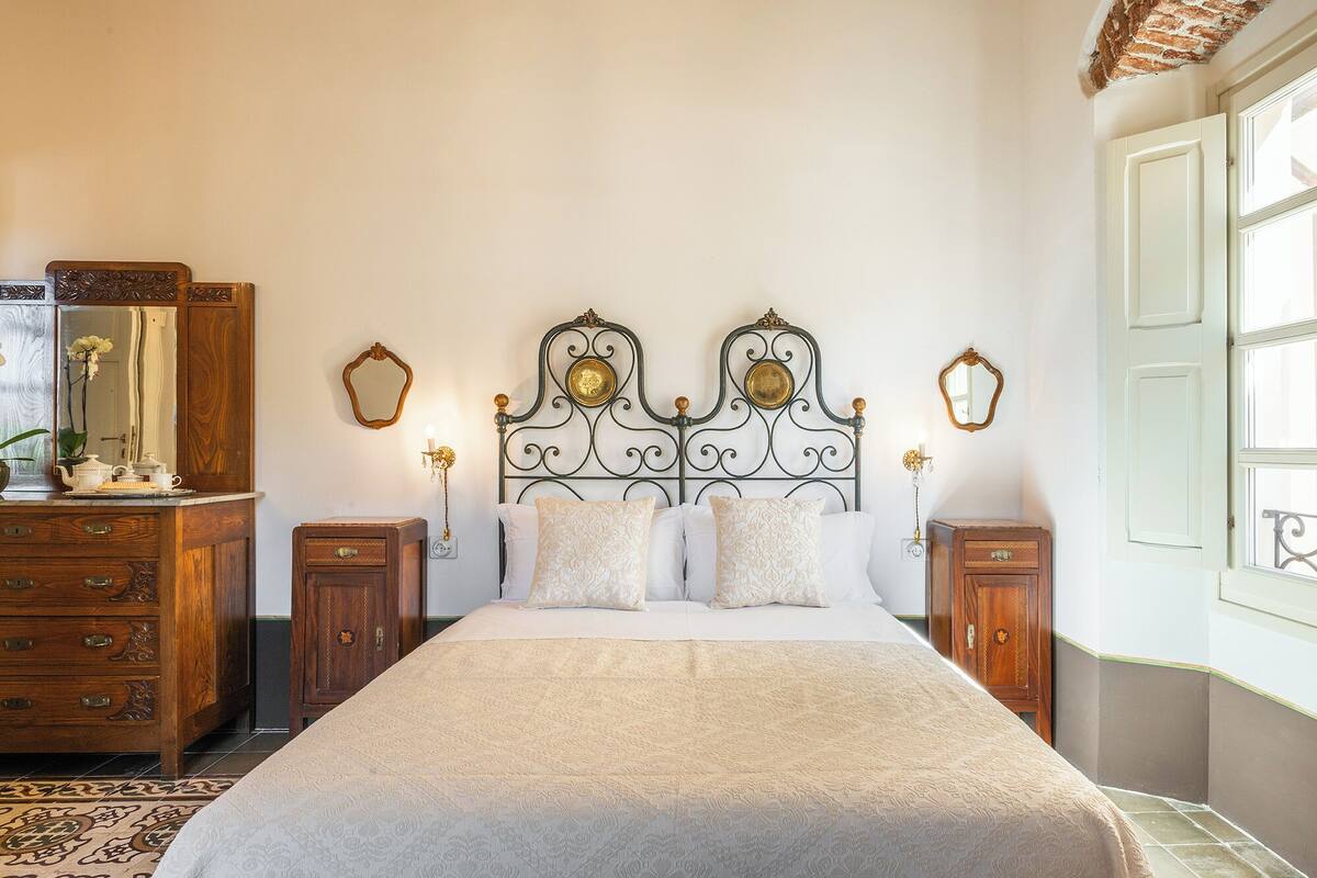 A bedroom with a large bed, wooden dresser, and two nightstands.