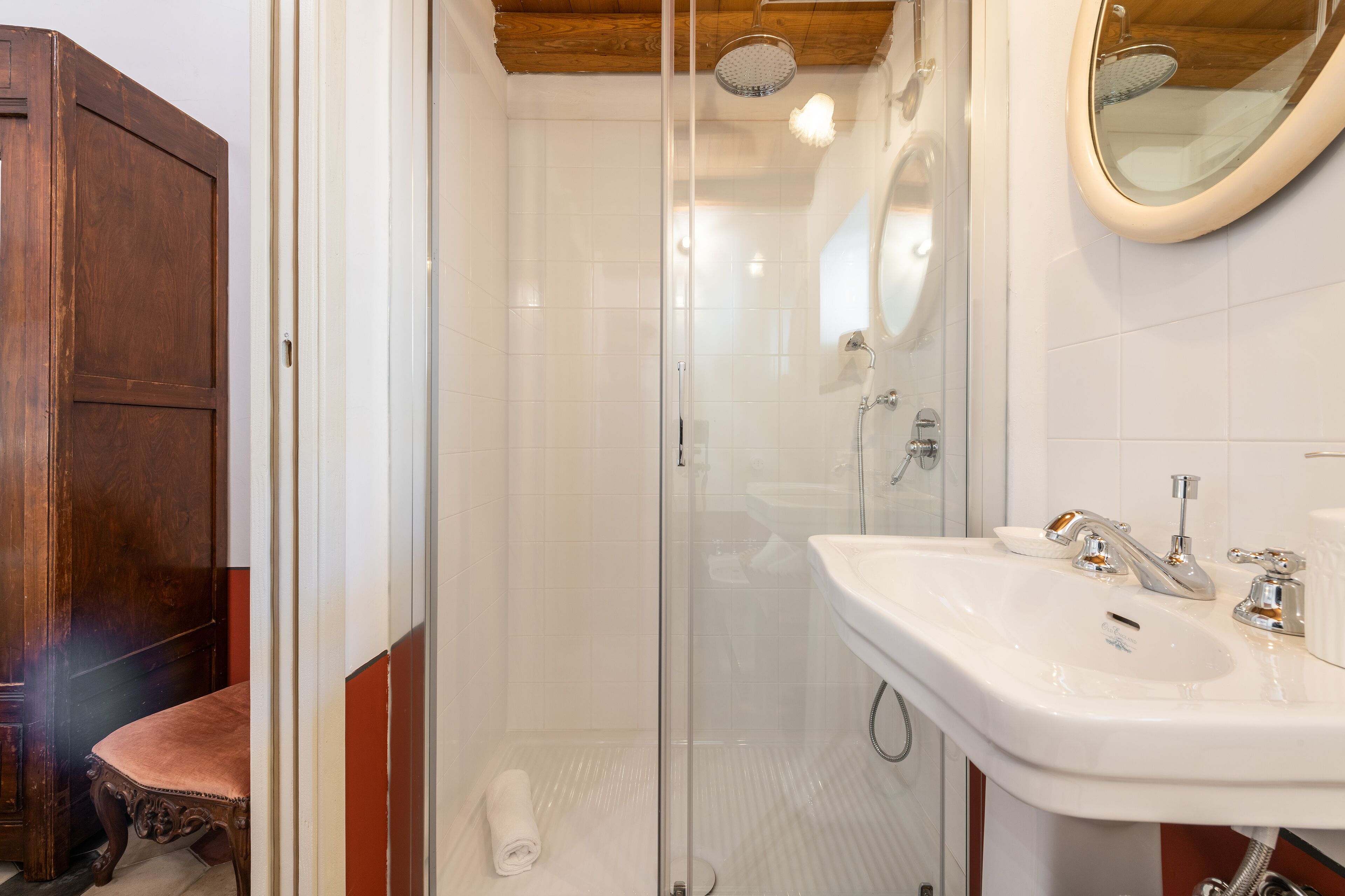 Un baño con ducha envuelta en vidrio, un lavabo blanco con dos grifos y un mueble de madera.