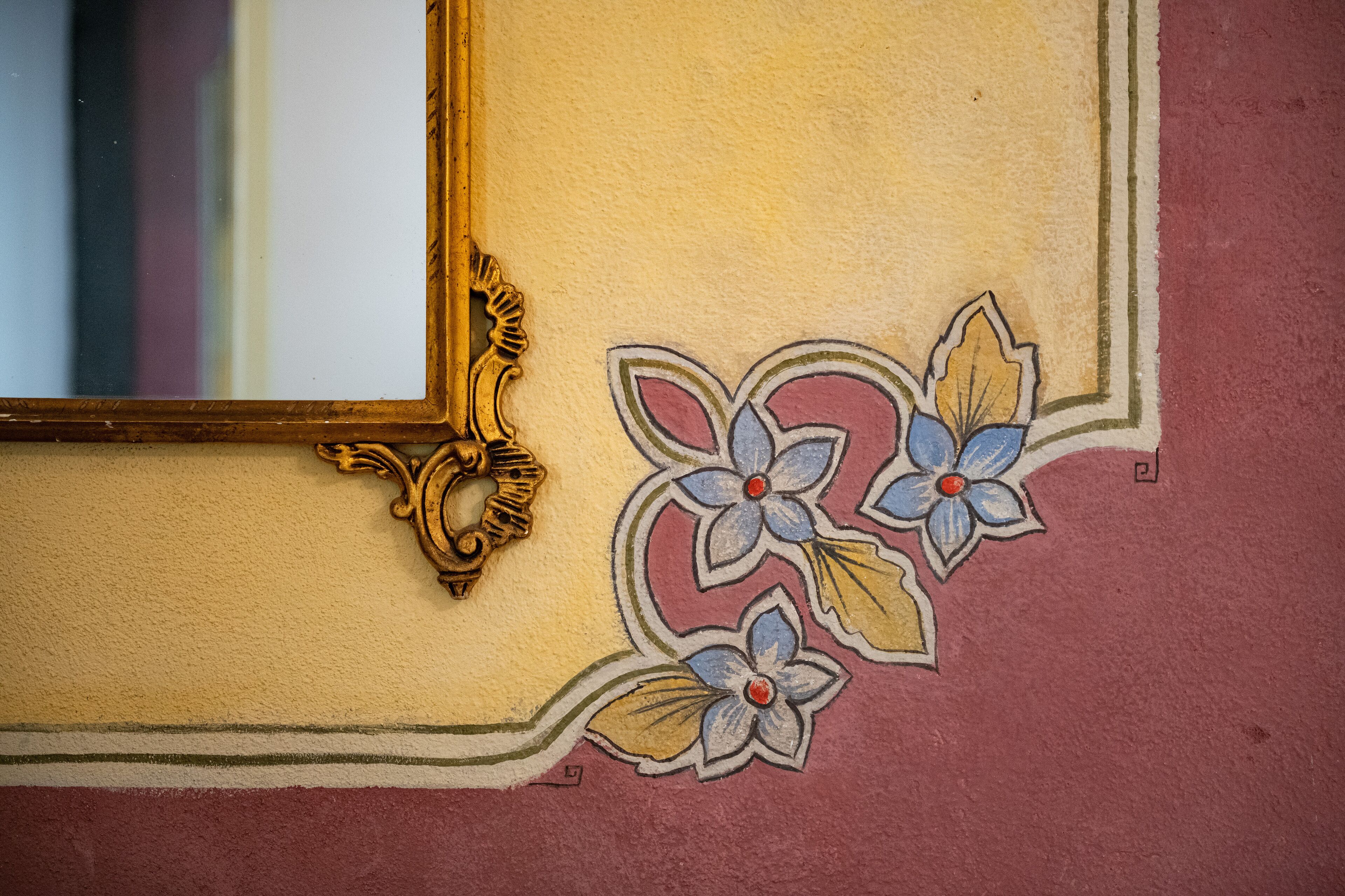Una pared con un estampado floral decorativo y un espejo con marco ornamentado.