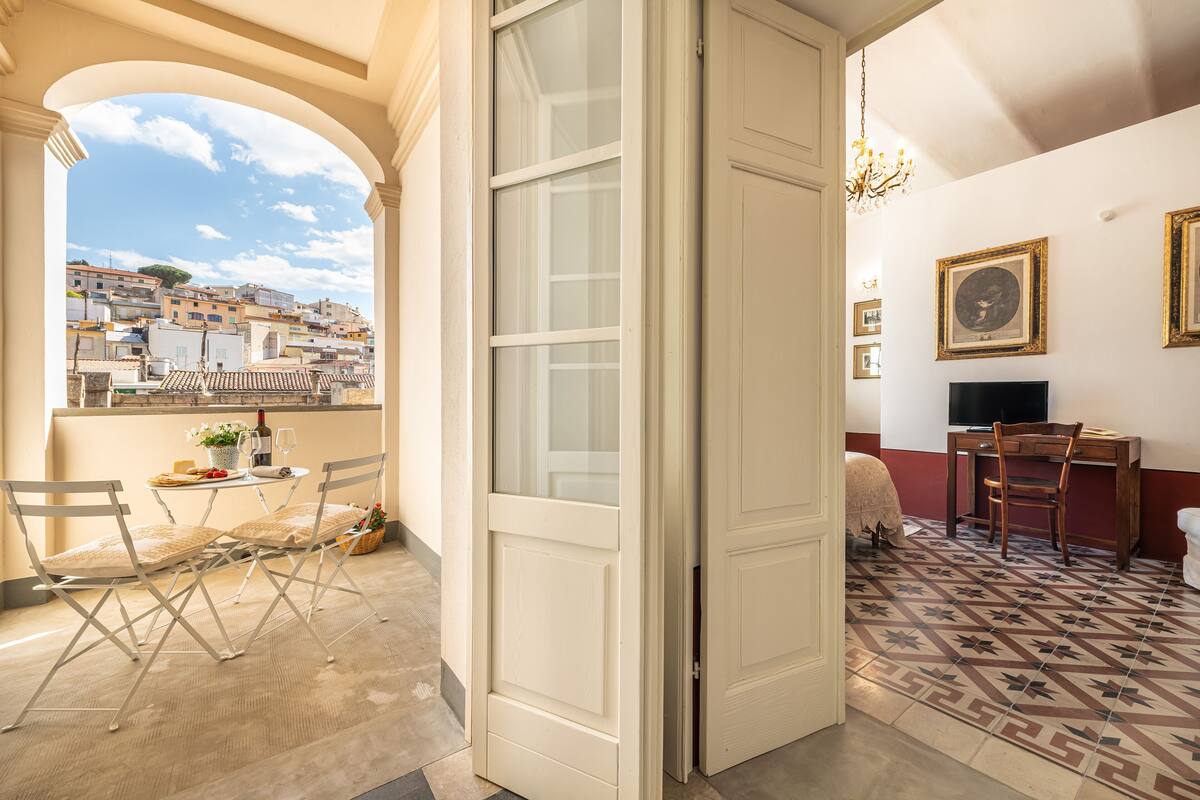A room with a balcony, a dining area with a table and chairs, a television, and a patterned floor.