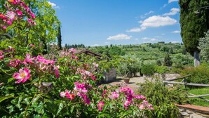 Um edifício rústico de pedra rodeado por vegetação exuberante e plantas floridas.