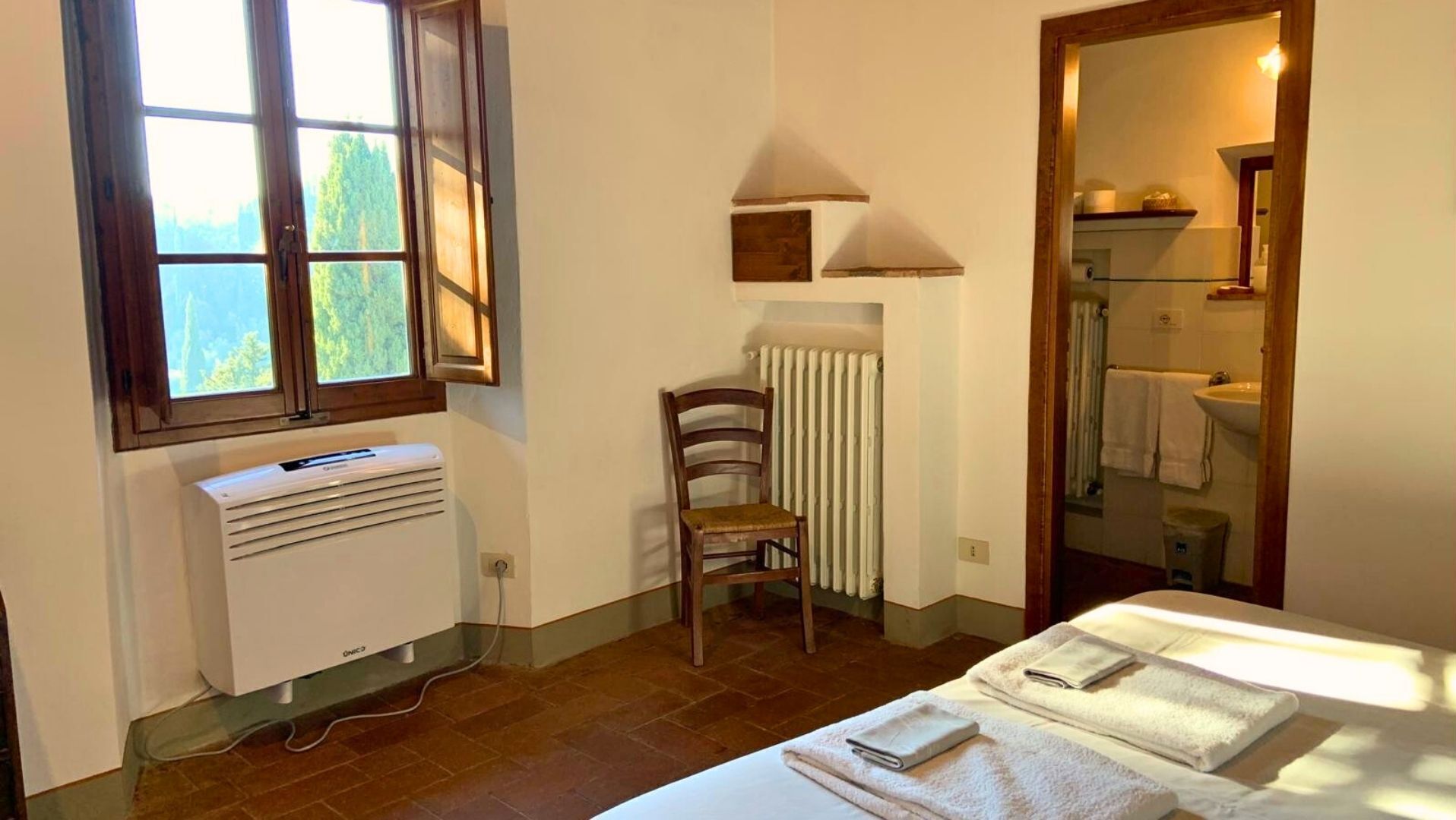Une chambre avec un radiateur, une chaise, un lit avec des serviettes, une fenêtre et un miroir.