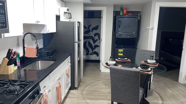 A modern kitchen with a gas stove, stainless steel appliances, a coffee maker, and a dining area with a glass table and chairs.