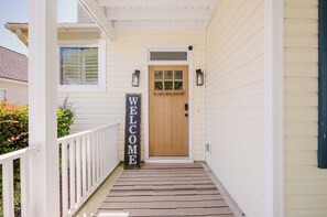 A house with a wooden front door, a welcome sign, and a porch with a white railing.