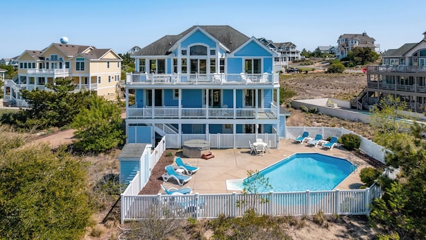 Una casa frente al mar de varios pisos con piscina, varios balcones y un patio amurallado.