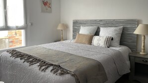 Un lit bien fait, avec une couvre-lit à motifs et des oreillers, une table de chevet avec une lampe, et une fenêtre avec des rideaux.