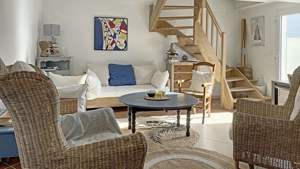 Un salon spacieux avec un plafond haut, un escalier en bois, une table basse ronde et des meubles en osier.