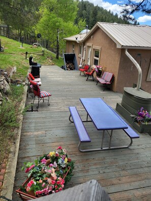 En träveranda med picknickbord och stolar, omgiven av krukväxter och en byggnad med ett sluttande tak.