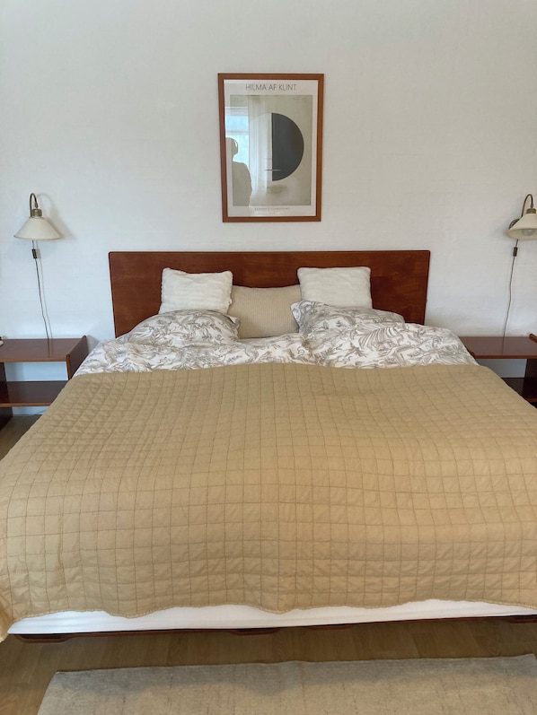 Una cama bien hecha con cubrecolchón acolchado, dos lámparas de noche y un cuadro en la pared.