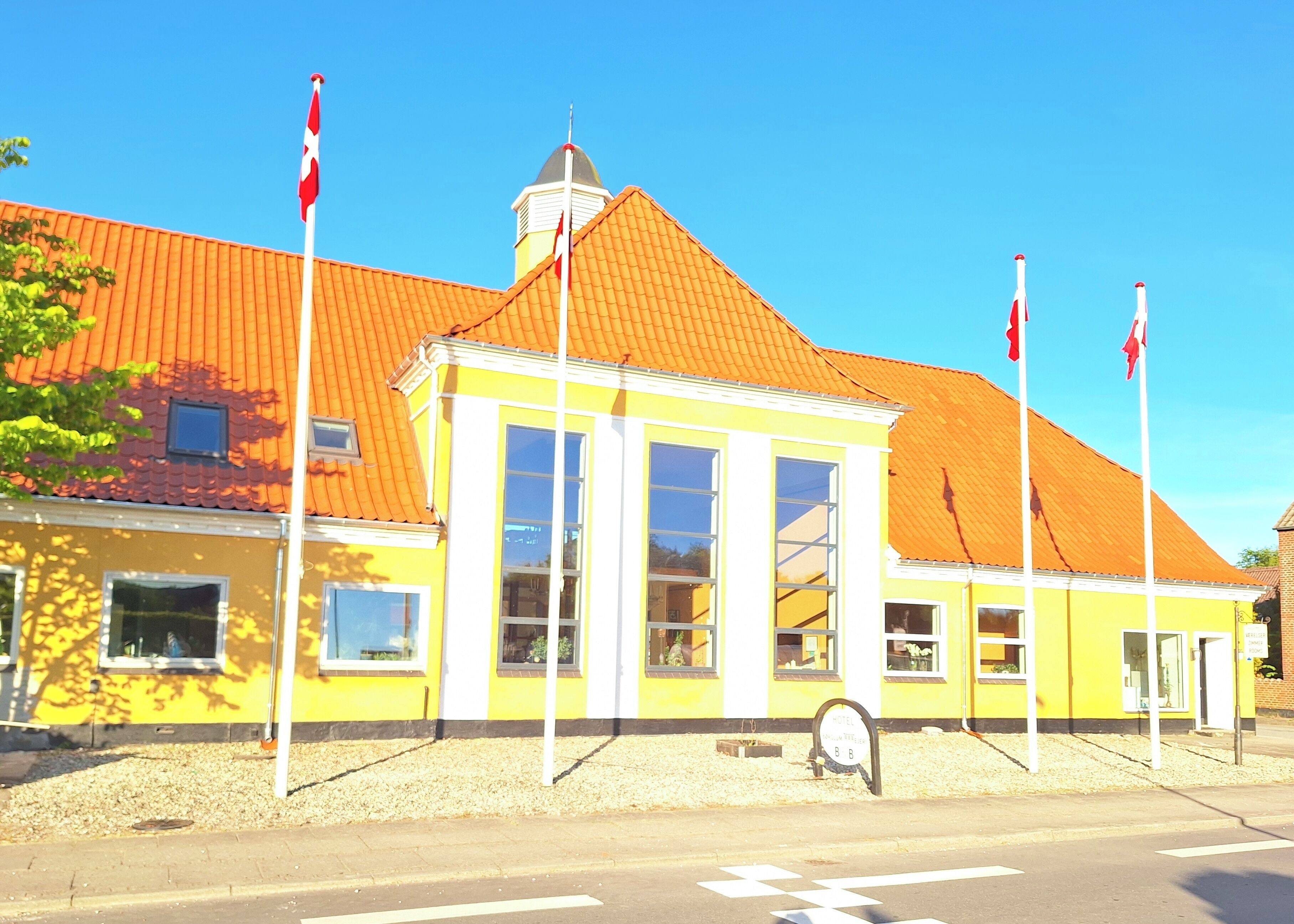 A yellow building with a red roof, large windows, and multiple flags.