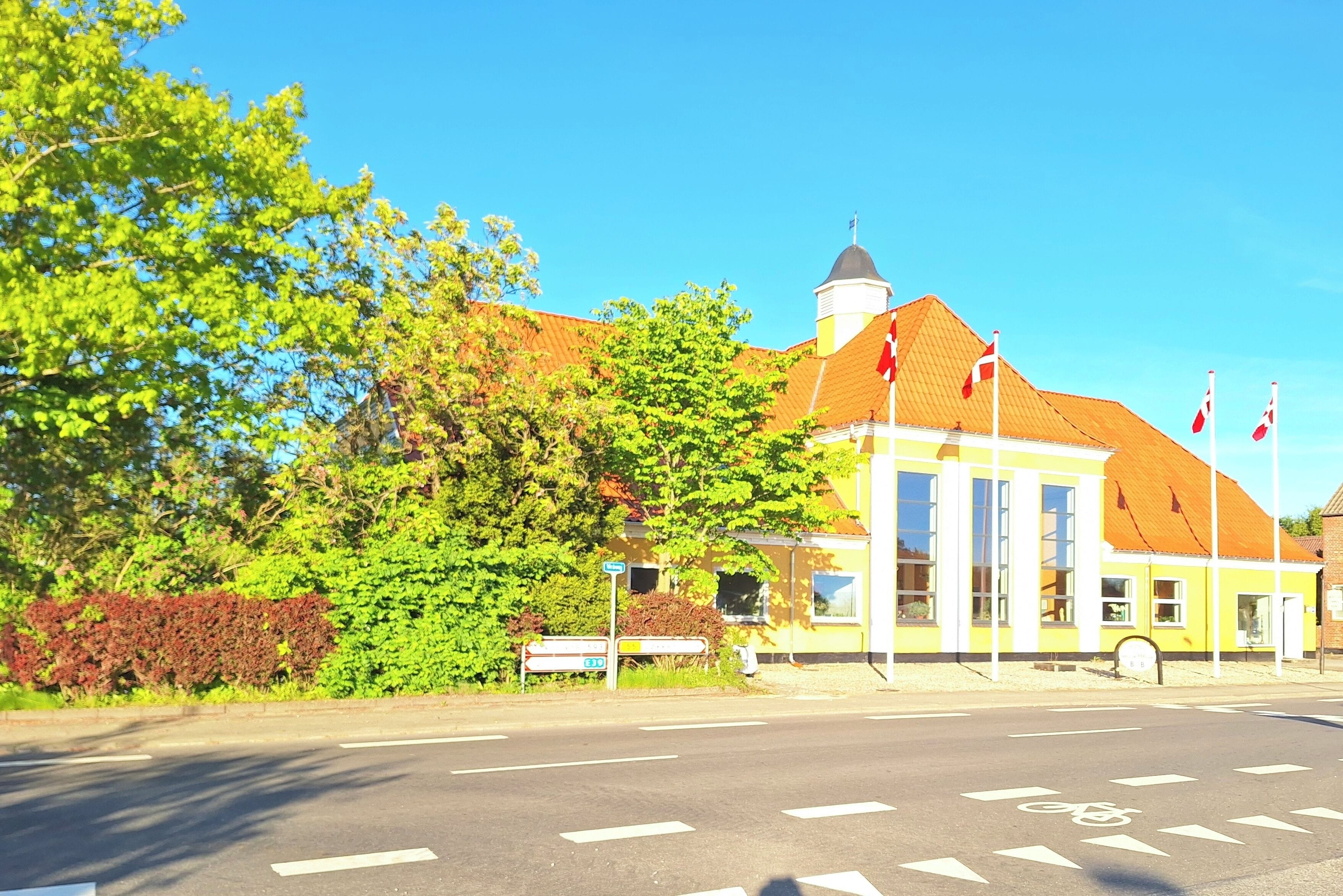 Ein Gebäude mit gelber Fassade und rotem Dach, eine Fahrradspur und ein klarer, blauer Himmel.